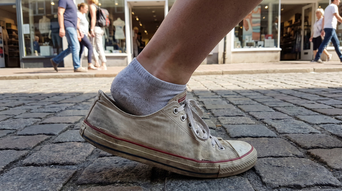 Foot lifting out of loose sneaker on cobblestone street — heel grips for shoes too big