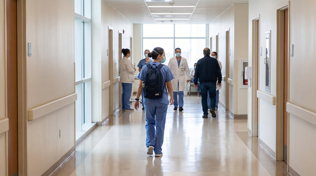 Nurse in scrubs walking down a hospital corridor, wide shot, bright clinical light