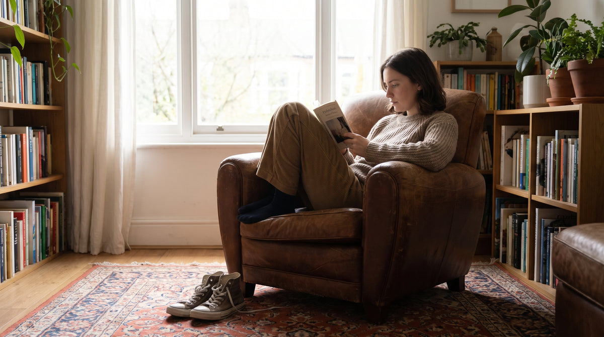 Person reading in an armchair by a window with shoes on the floor beside them